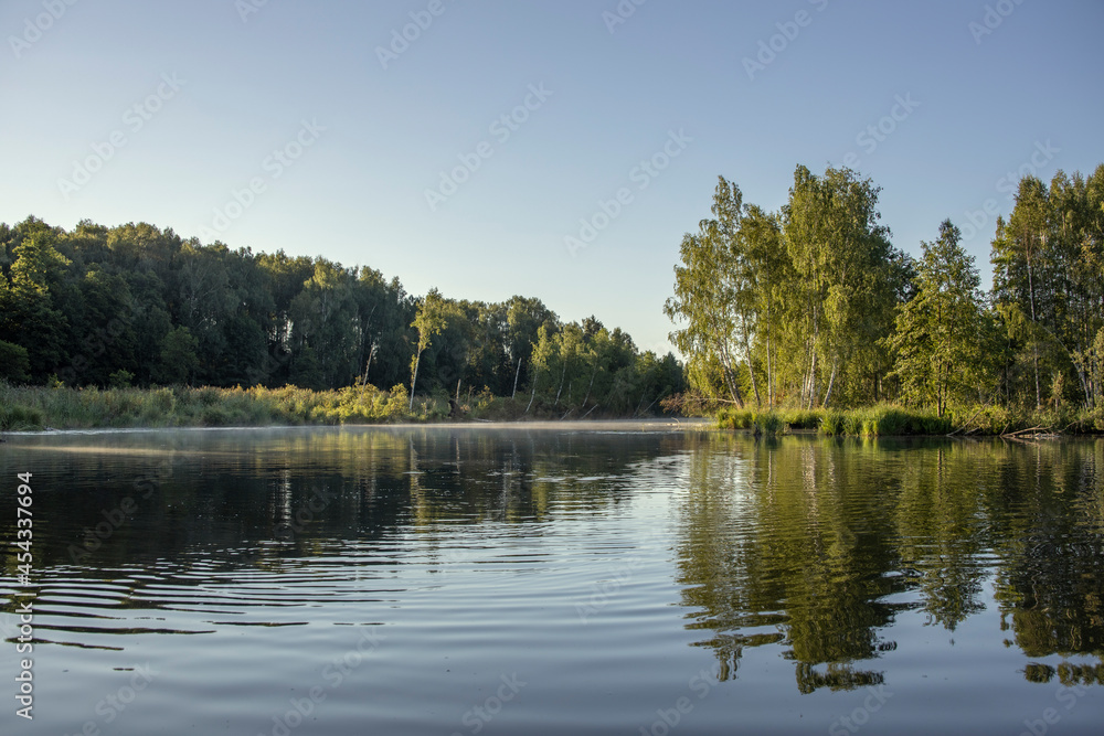 Picturesque landscape in the morning on the river. Sunbeams illuminate the trees at dawn. Kayaking early in the morning on a calm river in the summer.