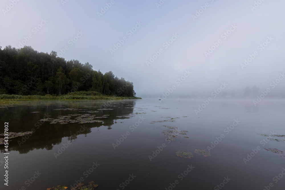 Mystical landscape at dawn. Early morning. Fog on the river. Beautiful dawn in the summer by the river. A man floats in a boat against the background of dawn. Mystical landscape at dawn. Early morning. Fog on the river. Beautiful dawn in the summer by the river. A man floats in a boat against the background of dawn.
