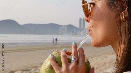 Woman drinking coconut water early morning at Balneário Camboriú, Brazil.