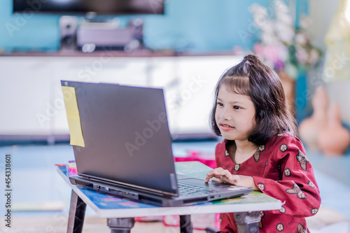 The girl at home communicates with friends on the Internet. Kids distance learning. Cute little girl using laptop at home. Education, online study, home studying, schoolgirl children lifestyle concept © Abdul