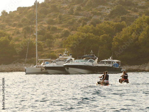 Two young couples ride jet skis along the lagoon near the yachts. Vacation nautical adventures. Fun on the water. The luxurious life of rich people. An extreme hobby of modern youth. Summer adventure photo