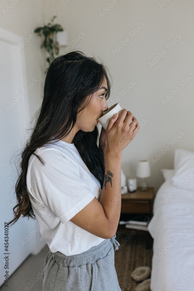 Woman standing and drinking coffee in bedroom