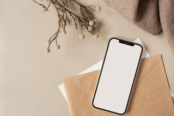 Blank clipping path screen mobile phone with mockup copy space and dry floral branch and blanket cloth on neutral beige background. Minimal aesthetic business brand template. Flat lay, top view