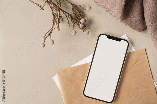Blank clipping path screen mobile phone with mockup copy space and dry floral branch and blanket cloth on neutral beige background. Minimal aesthetic business brand template. Flat lay, top view photo