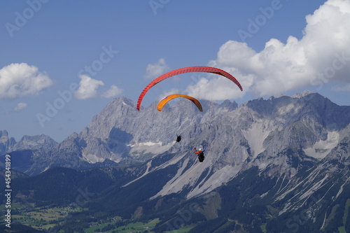 two friends paragliding over the vast alpine valley surrounded by the Austrian Alps of the Schladming-Dachstein region (Schladming, Austria)