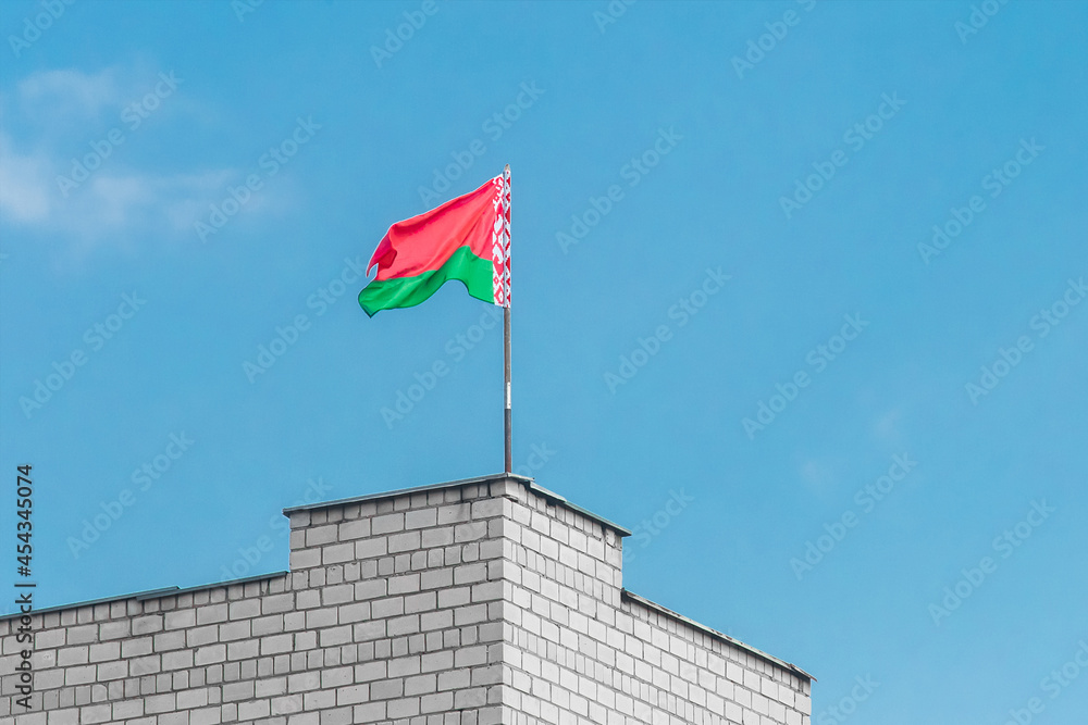 Belarusian flag on the edge of a brick building against a blue sky