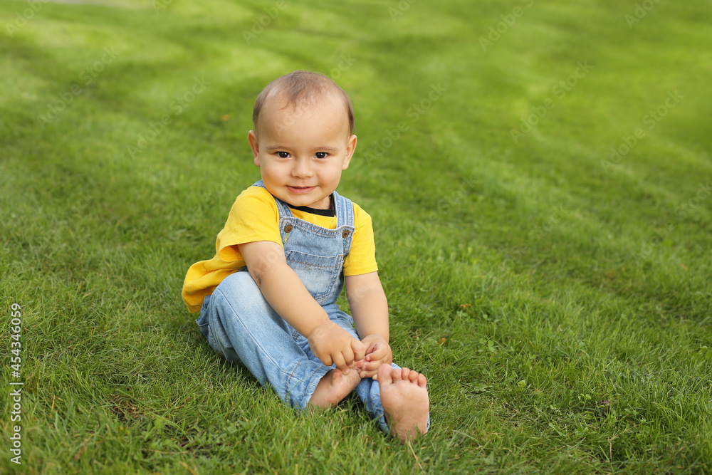 a beautiful little boy in a yellow T-shirt and a denim suit is sitting on the lawn in the park
a beautiful little boy in a yellow T-shirt and a denim suit is sitting on the lawn in the park