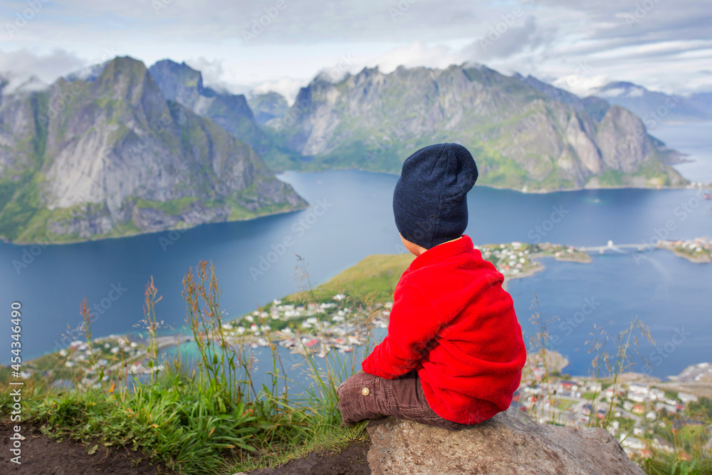 Cute child, standing on top of the mountains and looking down on Reine after climbing Reinebringen treeking path with lots of stairs Cute child, standing on top of the mountains and looking down on Reine after climbing Reinebringen treeking path with lots of stairs