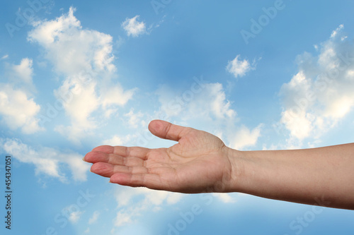 female hand outstretched against beautiful summer landscape, blue sky with clouds, concept of transcendence, infinity, height, the kingdom of God