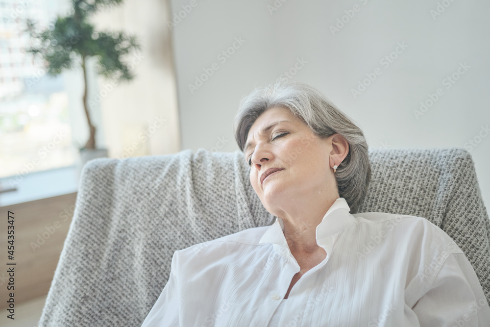 An elderly woman is snoozing in a comfortable chair, relaxing and