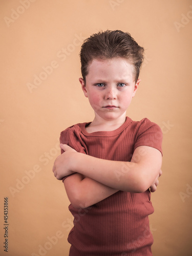 Annoyed boy with crossed arms on beige background
