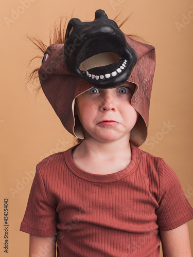 Fearful boy in horse mask on beige background