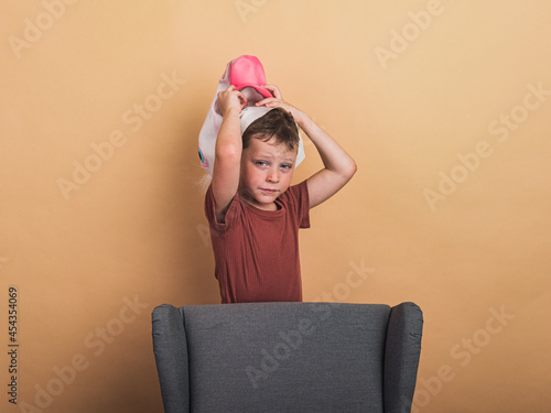 Tired boy taking off mask against armchair photo