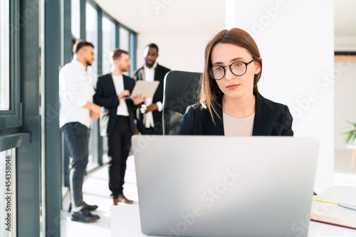Woman working in the office behind a laptop and her work colleagues in the background