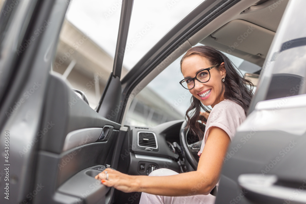 Smiling woman driver in glasses opens the car door looking backwards