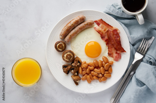 Horizontal flat lay of classic english keto breakfast. Full of protein and fat. Tasty sausages, delicious mushrooms, nutritious bacon, fried eggs, kidney beans, fresh orange juice and hot coffee