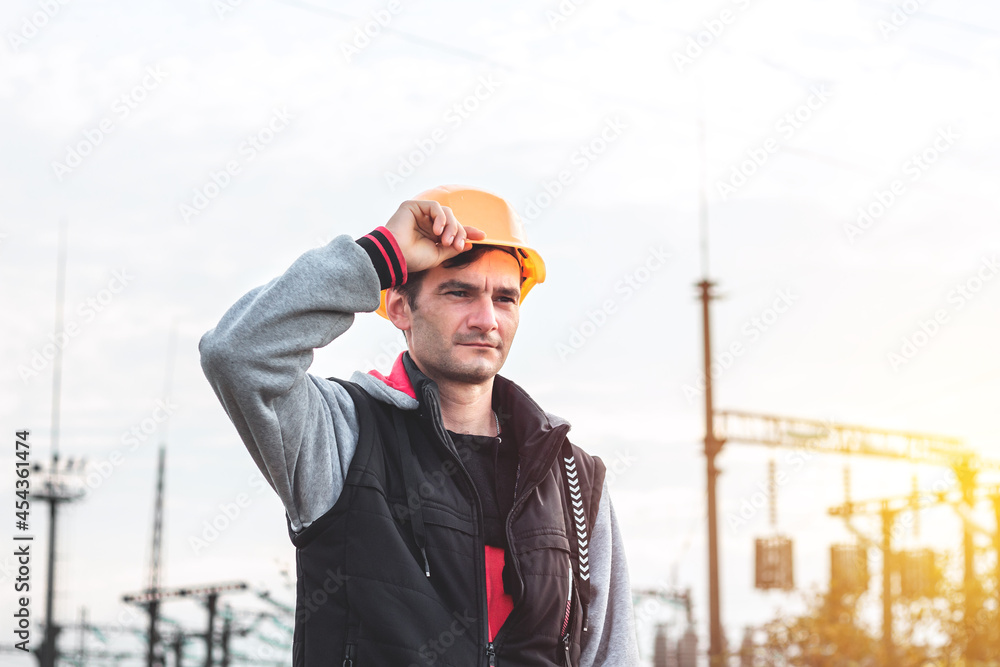 Worker in a helmet against the background of a substation and high-voltage poles Worker in a helmet against the background of a substation and high-voltage poles