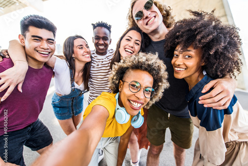 Multicultural happy friends having fun taking group selfie portrait on city street - Multiracial young people celebrating laughing together outdoors - Happy lifestyle concept. photo