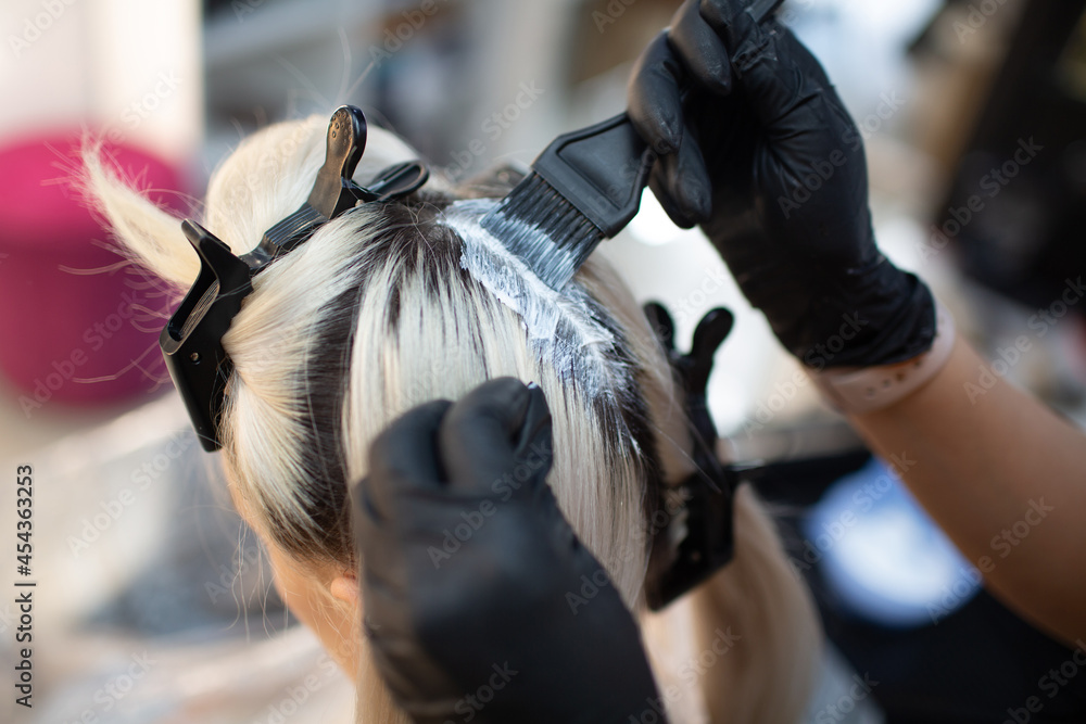 Young woman hairdresser dying hair at beauty salon. Professional hair roots coloring.