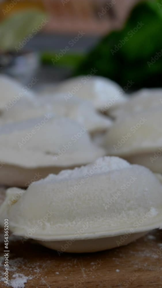 Rows of frozen raw pelmeni dumplings stuffed with mince meat on cutting board. Delicious traditional handmade food on domestic kitchen. Asian and russian cuisine. Vertical video. Rows of frozen raw pelmeni dumplings stuffed with mince meat on cutting board. Delicious traditional handmade food on domestic kitchen. Asian and russian cuisine. Vertical video.