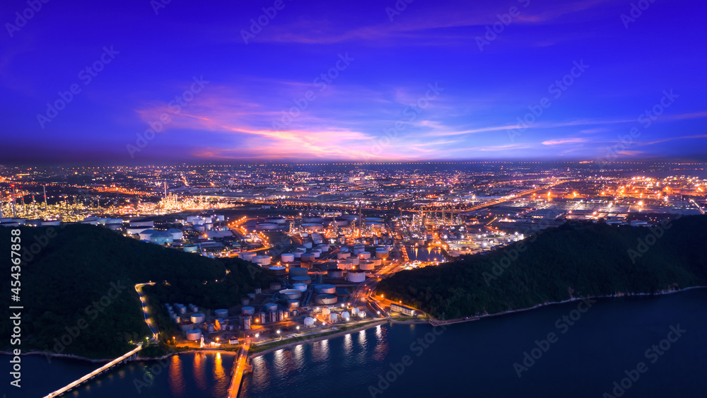 twilight landscape oil and gas LPG refinery factory with storage tanks area zone on island industry business import and export at night over lighting blue cloud sky background and the sea in front