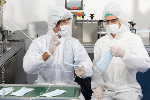 male engineers wearing personal protective equipment uniform(PPE) wearing medical face mask, producing medical face masks and ok pose beside machine in laboratory