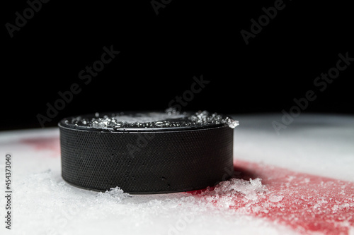 Black hockey puck on the ice rink, with painted red line.