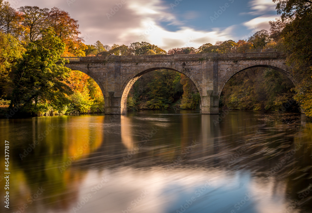A long exposure of a beautiful arched bridge near Durham Cathedral with the autumn colors reflecting in the River Wear