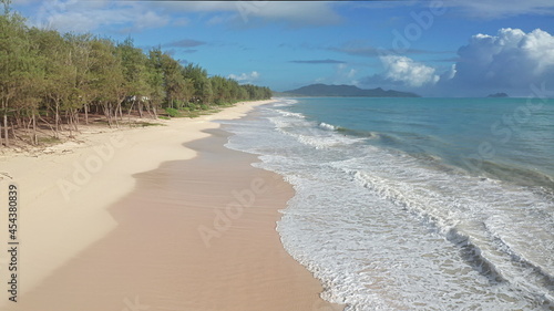 Colorful Aerial View of tropical beach with turquoise blue ocean water and waves lapping on hidden white sand beach. Blue skies with green trees vegetation. Waimanalo Beach  Oahu Hawaii Island. 4k.