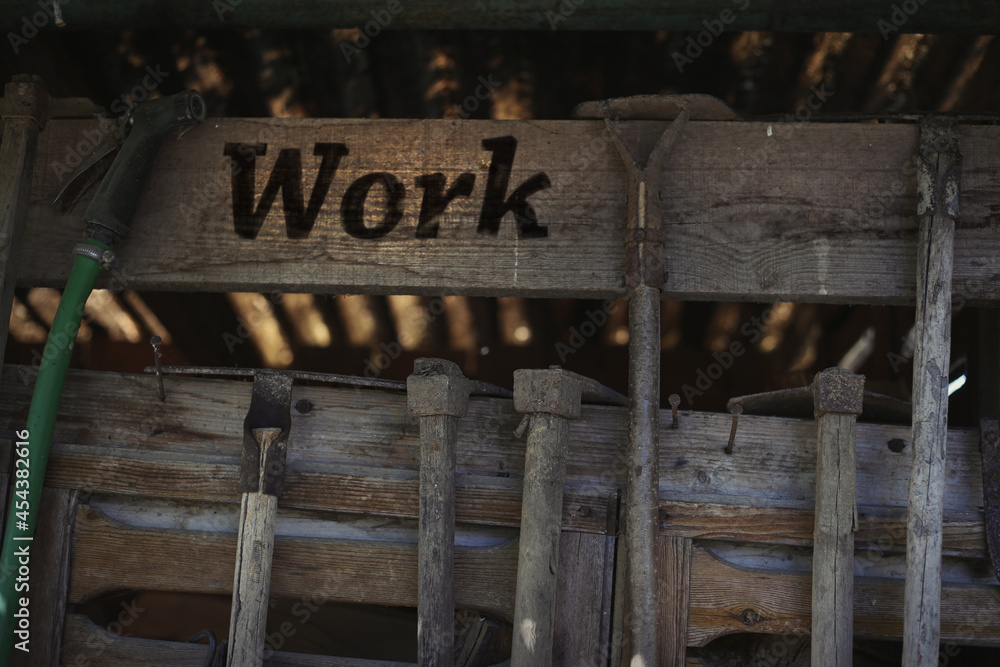 Old wooden vintage workshop with working tools and the text Work. Gardening tools hanging on a wooden grunge shed, garden maintenance concept