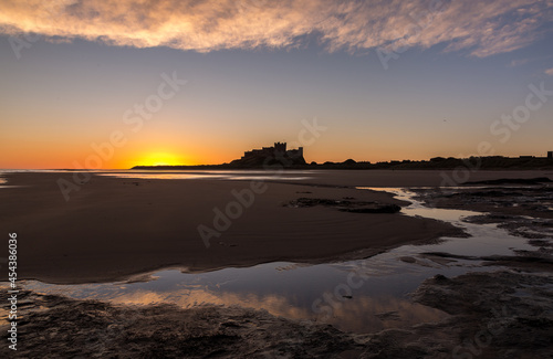 The iconic Bamburgh Castle in Northumberland at sunrise  with the nearby beach deserted. 