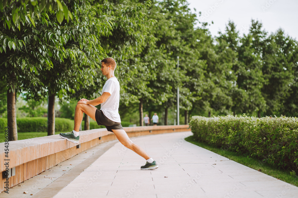Attractive man athlete wearing sportswear do stretching exercises in modern park at summer morning