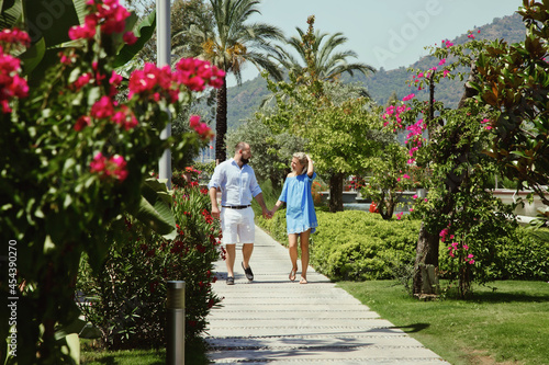 Loving couple enjoying honeymoon in luxury hotel, walking through grounds with palm trees and beauty flowers. Happy lovers on romantic trip have fun on summer vacation. Concept romance and relaxation © Alex Vog
