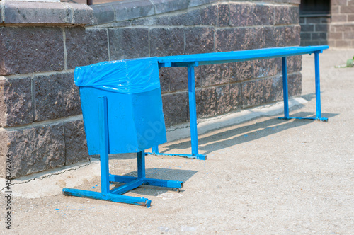 an iron garbage can and a blue bench near a residential building. Improvement of public space in an urban environment, a place for recreation. There are no people, it's a sunny day.