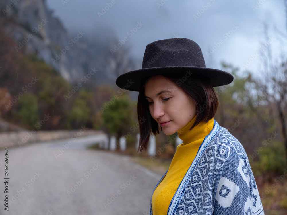 Stylish hipster woman in hat and poncho walking down a mountain road. The concept of travel and wanderlust. An amazing atmospheric moment