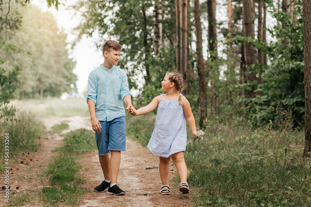 A boy and a girl, brother and sister walk along a forest path together A boy and a girl, brother and sister walk along a forest path together