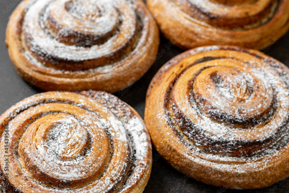 Sweet spiral bun with poppy seeds and powdered sugar large on a dark background. Delicious yeast pastries close-up. The concept of homemade high-calorie pastries