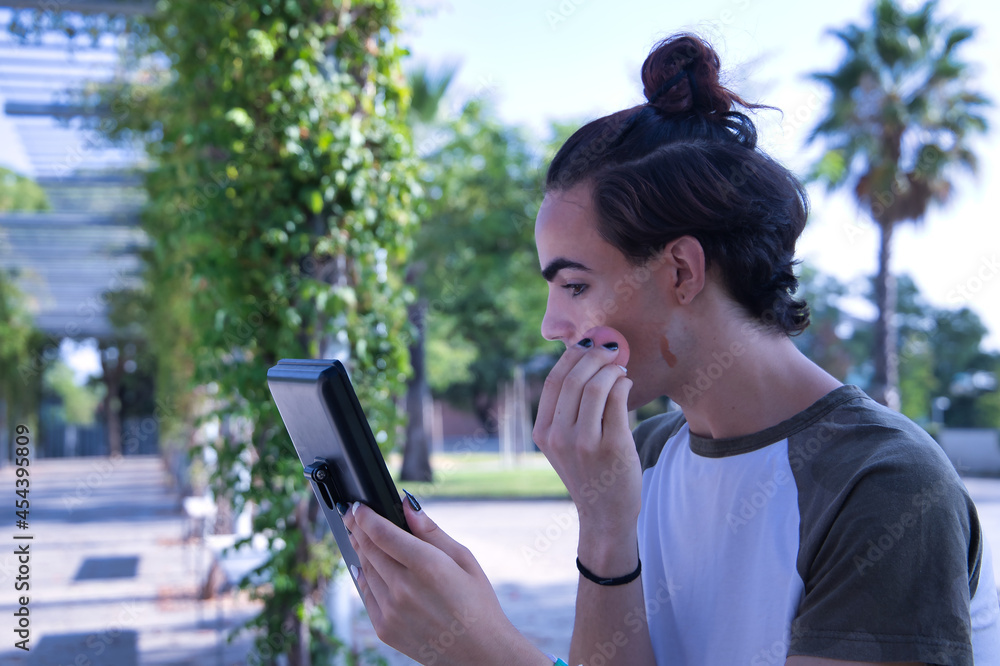Young adult Hispanic transsexual girl doing her makeup in front of a hand mirror. Concept of transsexuality, inclusion and diversity. Young adult Hispanic transsexual girl doing her makeup in front of a hand mirror. Concept of transsexuality, inclusion and diversity.