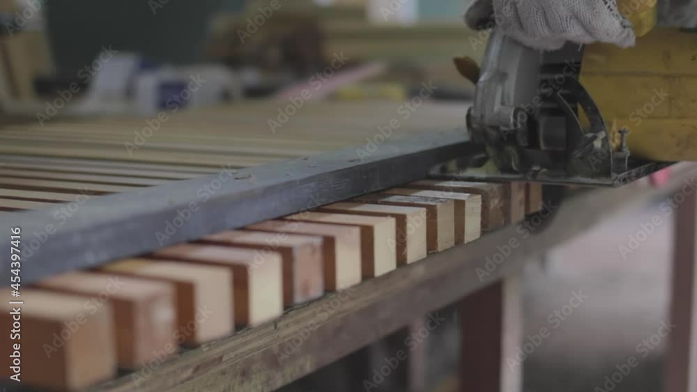 Closeup of joiner cutting square decorative wood rods with electric circular saw