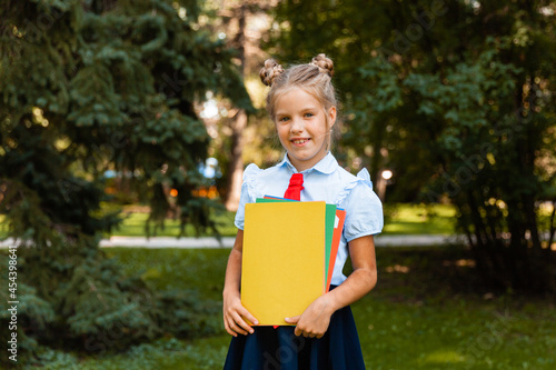 Happy schoolgirl holding a book outdoors. A small child goes to school. Copy space. photo