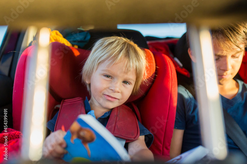 Children, traveling to vacation with car, sitting in carseats and reading books and playing on mobile photo