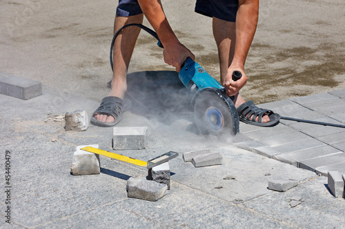 A builder cuts granite slabs and paving slabs with a diamond disc to arrange the sidewalk.