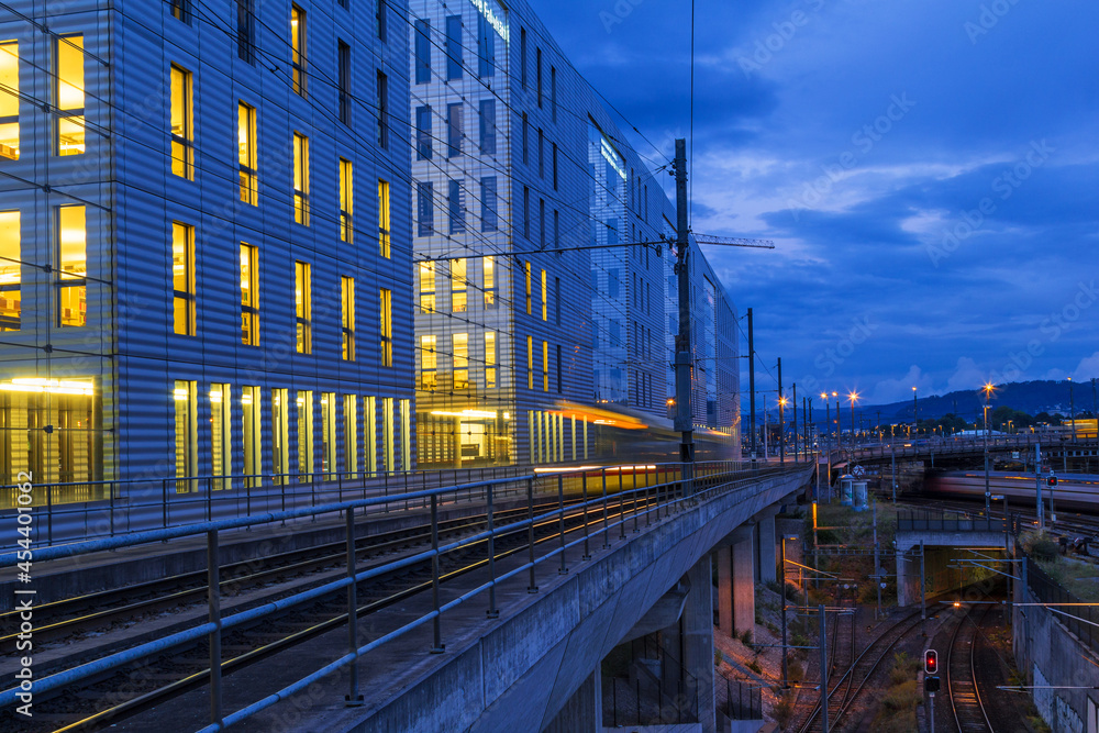 Basel, Switzerland -  August 30. 2021: The Jacob Burckhardt Building in the twilight hour with a tram passing by. The modern building complex houses business companies and educational institutes.