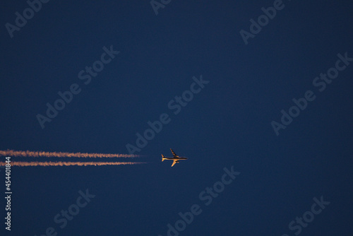 Beautiful telephoto evening view of airplane contrail in orange colors of setting Sun on dark blue background seen over Dublin Mountains, Ireland. Golden hour minimalism concept
