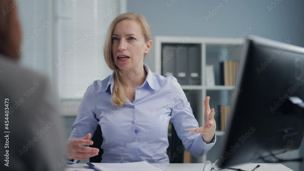 Angry female director sitting at desk and throwing papers around while shouting on mature woman. Business lady screaming on employee because of failure at work. Angry female director sitting at desk and throwing papers around while shouting on mature woman. Business lady screaming on employee because of failure at work.