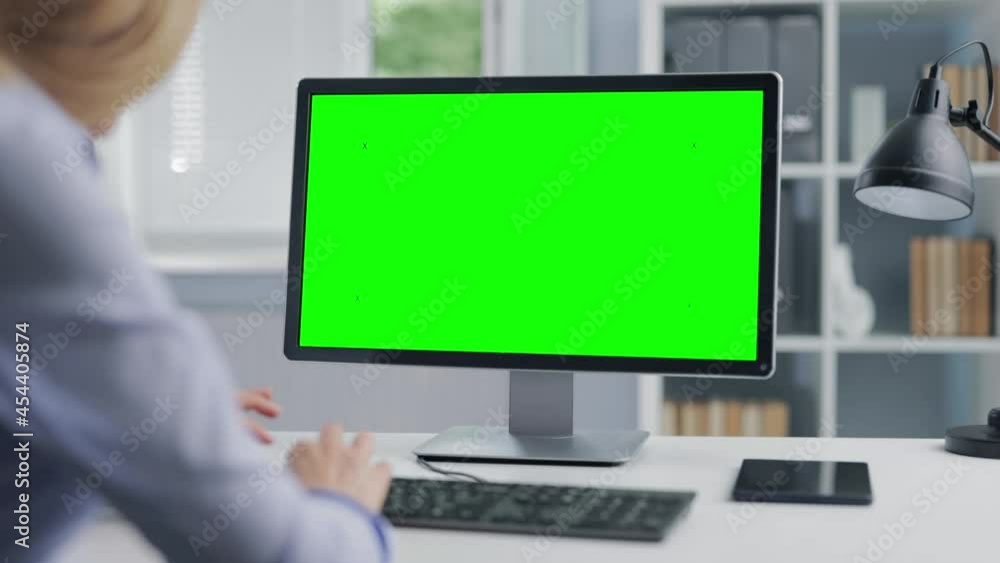 Back view of mature lady in formal clothes working on computer with chroma key screen while sitting at bright office. Concept of people and technology. Back view of mature lady in formal clothes working on computer with chroma key screen while sitting at bright office. Concept of people and technology.