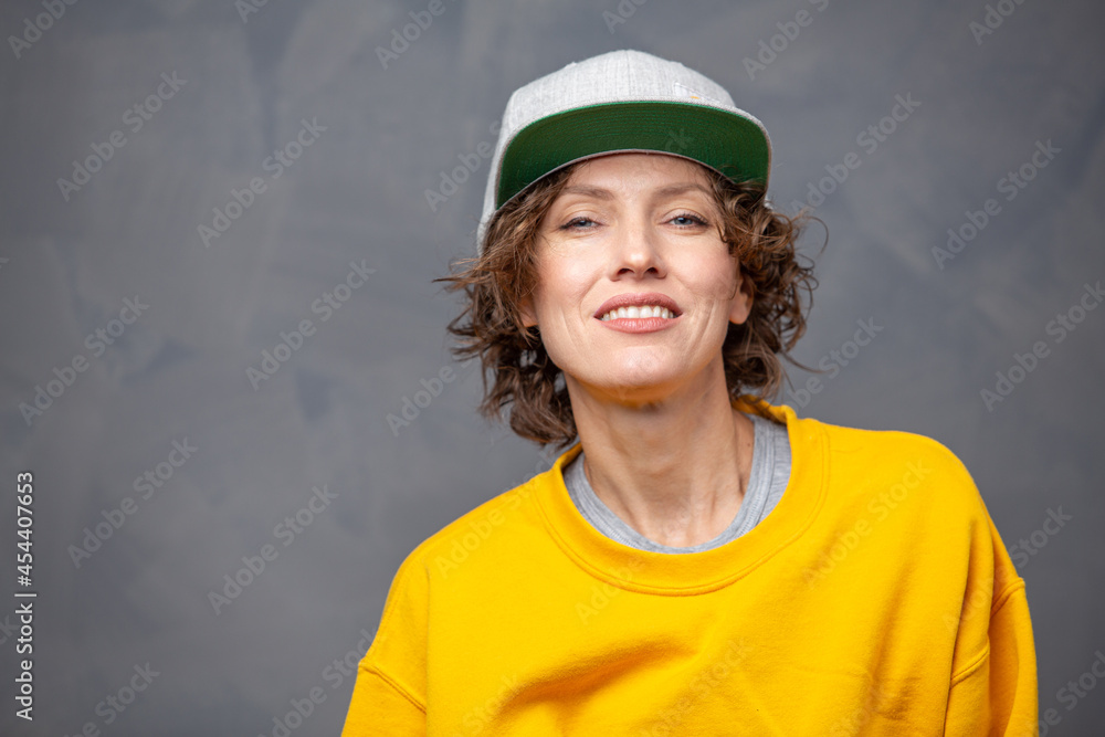 Autumn mood! Portrait of happy smiling woman with short brunette curly hair wearing yellow sweater and a hat over grey wall background Autumn mood! Portrait of happy smiling woman with short brunette curly hair wearing yellow sweater and a hat over grey wall background
