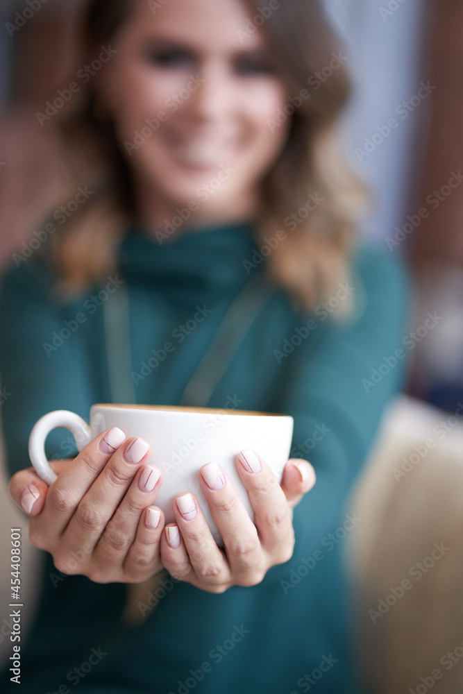 Blurred background. A beautiful woman with a beautiful manicure holds a cup of coffee and stretches it forward. She looks directly at the camera with a smile. High quality photo Blurred background. A beautiful woman with a beautiful manicure holds a cup of coffee and stretches it forward. She looks directly at the camera with a smile. High quality photo