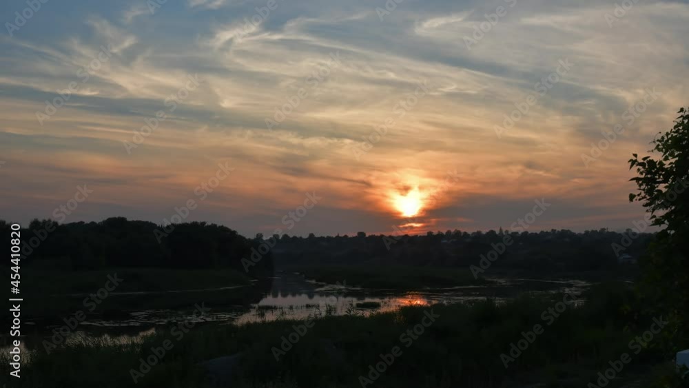 Cloudscape sunset time lapse. Cirrus clouds in sky over Southern Bug river shore with sun reflection in rippled water overgrown by reeds and bulrush plants. Tranquil landscape sundown Cloudscape sunset time lapse. Cirrus clouds in sky over Southern Bug river shore with sun reflection in rippled water overgrown by reeds and bulrush plants. Tranquil landscape sundown