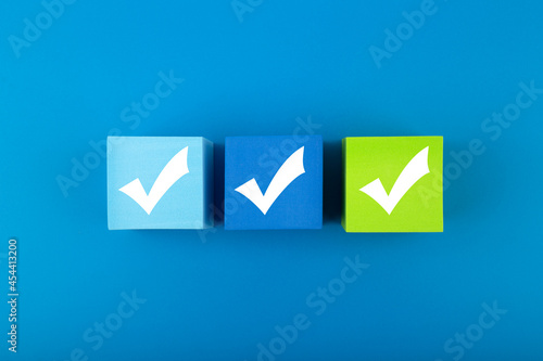 Creative flat lay with three checkmarks close up on blue and green toy cubes in the middle of blue background. Concept of questionary, checklist, to do list, planning or business plans